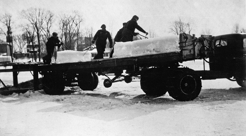 Black and white photograph of a trailer onto which four men are loading huge blocks of ice.