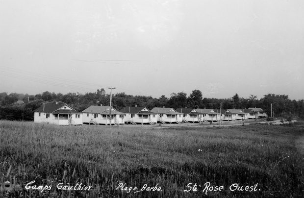 Black and white photograph of a group of small identical white wooden cottages, built side by side.