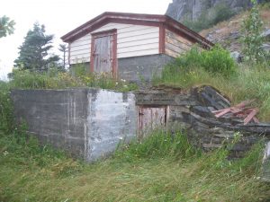 Cave à légumes avec deux entrées, surplombée par une remise blanche avec une porte et un toit rouges.