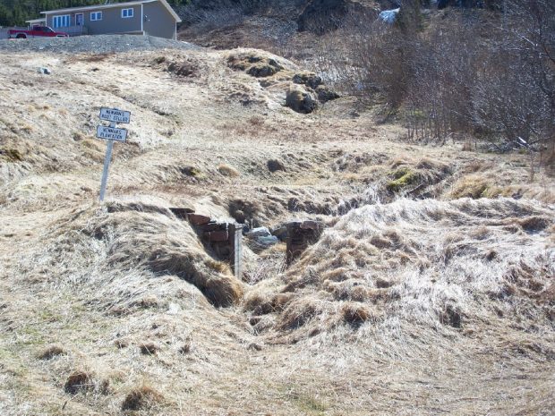 Crumbled ruins of the stone foundations of a root cellar in a grassy field.