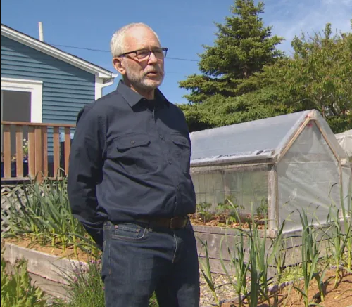 Dan Rubin standing in front of a backyard garden and greenhouse.