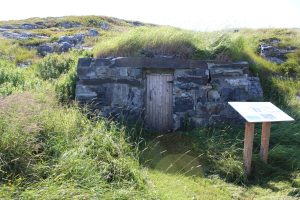 Hillside root cellar with a square wood door on a stacked stone façade on a grassy hillside.