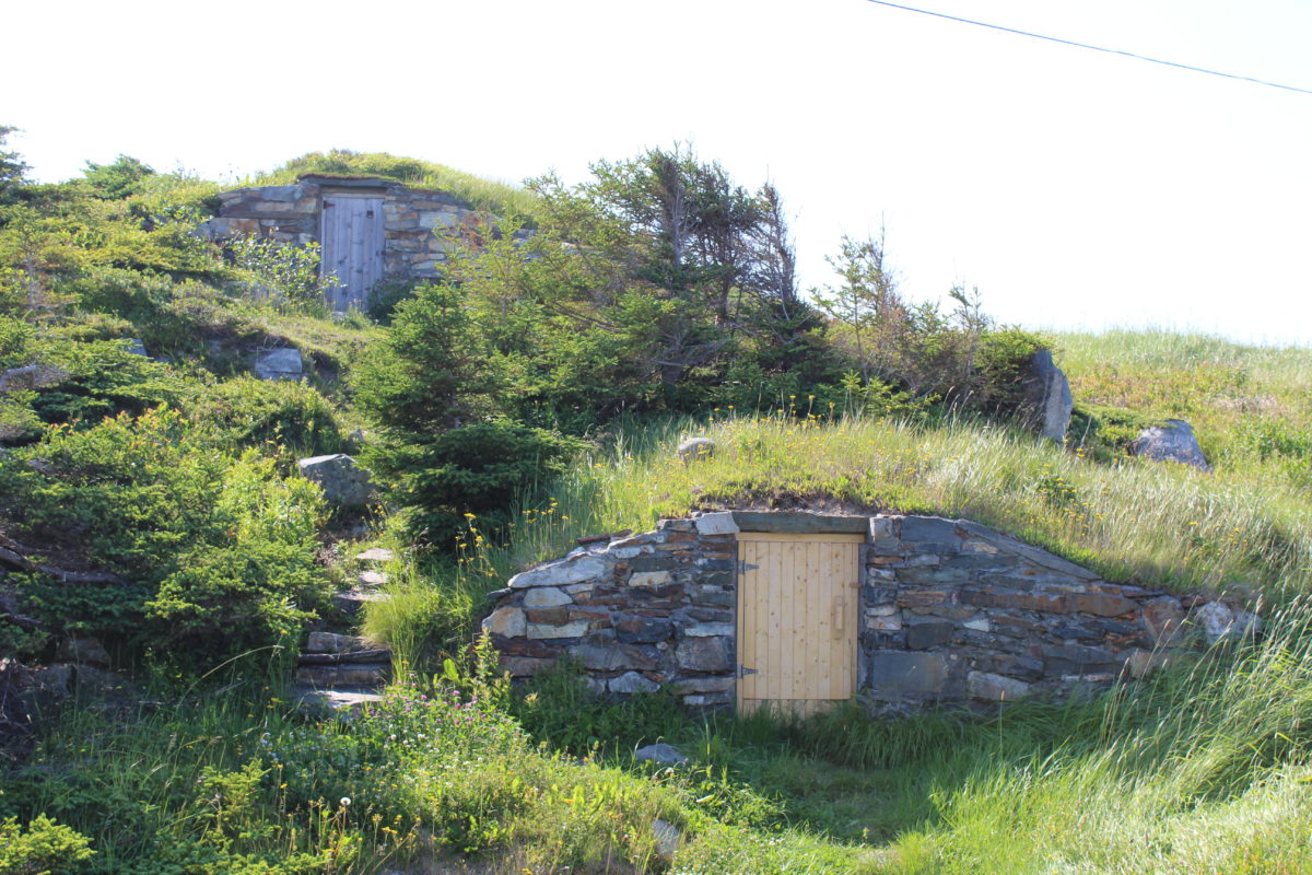 Exterior of two stacked stone hillside root cellars with small wooden doors.