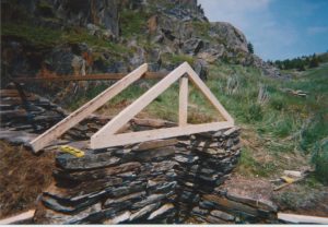  Pierres empilées à flanc de colline, sans porte, avec la structure de la remise au-dessus en cours de construction.