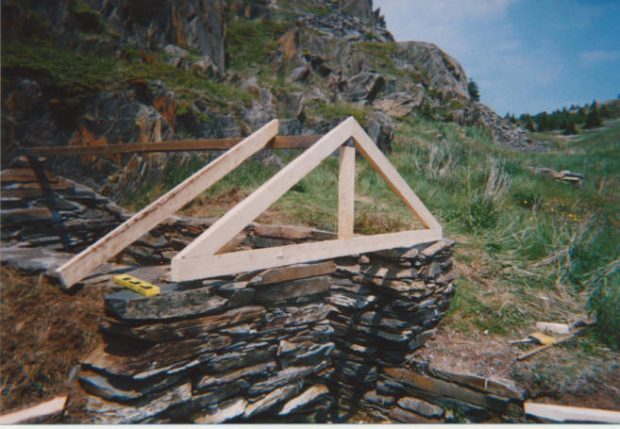 Stone stacked hillside root cellar with no door and the top shed structure in the works of being constructed.