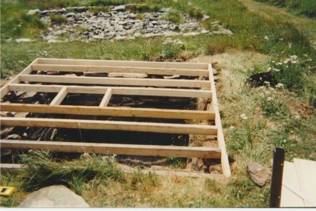 Structural component of the root cellar ceiling/top shed floor being constructed with wooden beams.