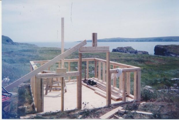 The structural foundations of the wooden top shed of the root cellar in a grassy field by the ocean.