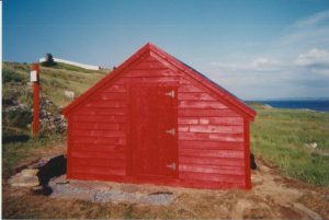 Exterior of red top shed of a root cellar in a grassy field.