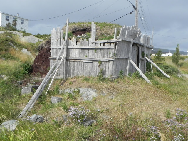 Square wooden structure with brace in a grassy field with a grass-covered top.