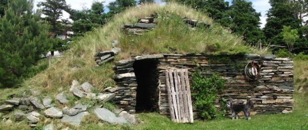 Exterior of a hillside root cellar with a stacked stone front and grass ontop.