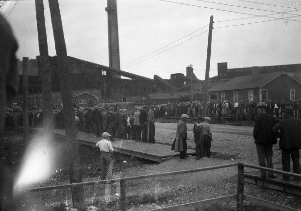Black-and-white photograph of people gathered on two opposite sidewalks in front of the Horne smelter.