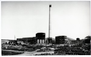 Black-and-white photograph of the construction of the Horne smelter. You can see a chimney in the middle, and many building materials in the foreground.