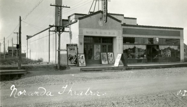 Black-and-white photograph of a building with Noranda written on the front. Several movie posters are hung on the boardwalk.