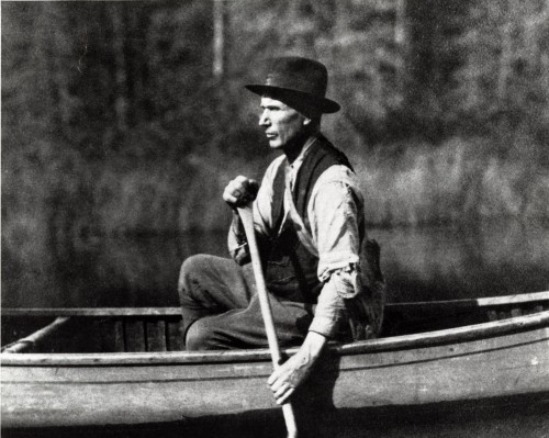 Black-and-white photograph of prospector Edmund Horne paddling on a lake with the forest in the background.