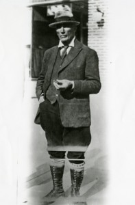 Photographie en noir et blanc du prospecteur habillé en costume cravate avec des bottes hautes et un cigare dans les mains.