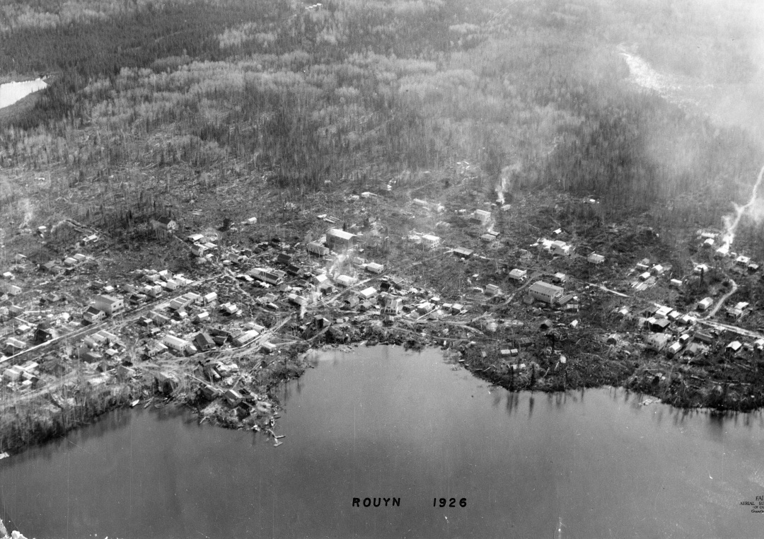 Black-and-white photograph of approximately 100 log cabins built in a chaotic way on the shores of Osisko Lake.
