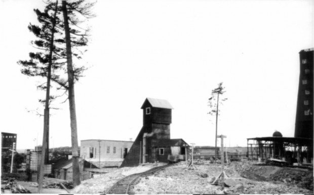 Black-and-white photography of a rudimentary railway with some trees and several buildings.