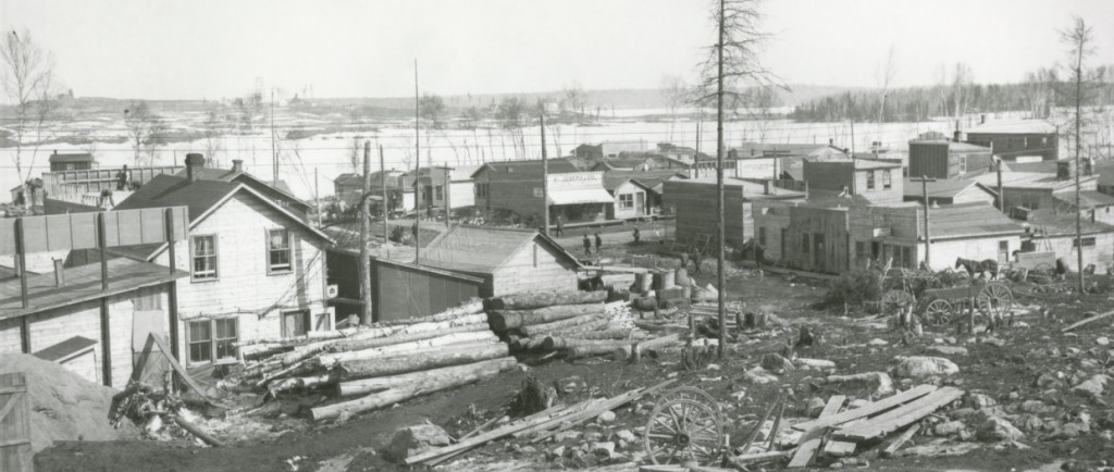 Black-and-white photograph of rudimentary buildings southwest of Osisko Lake. In the background, you can see rocks, timbers, wooden planks and waste.