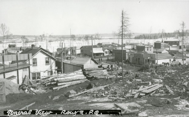 Black-and-white photograph of rudimentary buildings southwest of Osisko Lake. In the background, you can see rocks, timbers, wooden planks and waste.