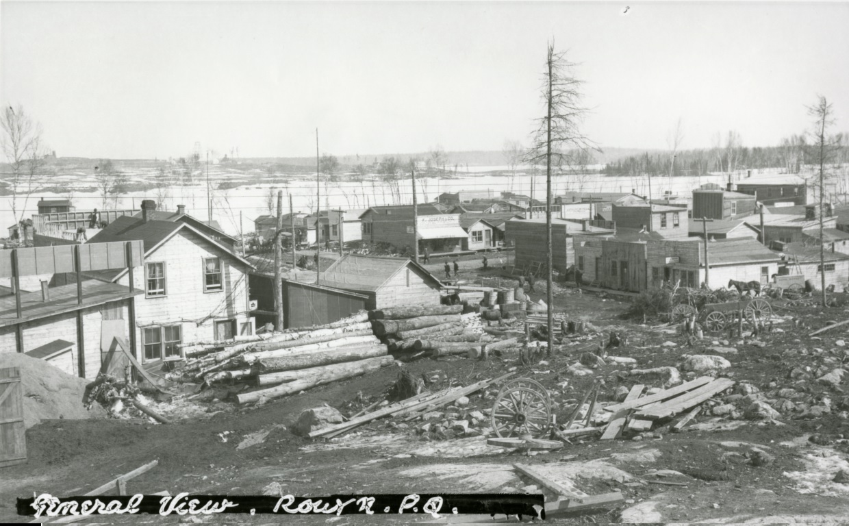 Black-and-white photograph of rudimentary buildings southwest of Osisko Lake. In the background, you can see rocks, timbers, wooden planks and waste.