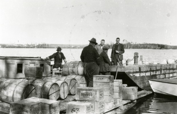 Black-and-white photograph of five men on a dock in the process of unloading crates and wood barrels.