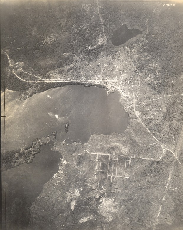 Black-and-white photograph, taken from a plane, of Rouyn and Noranda in their early days. A lake is in the middle of the photo. It is hard to see details from this height, but you can still see that the city of Rouyn is more populated than its neighbour Noranda.