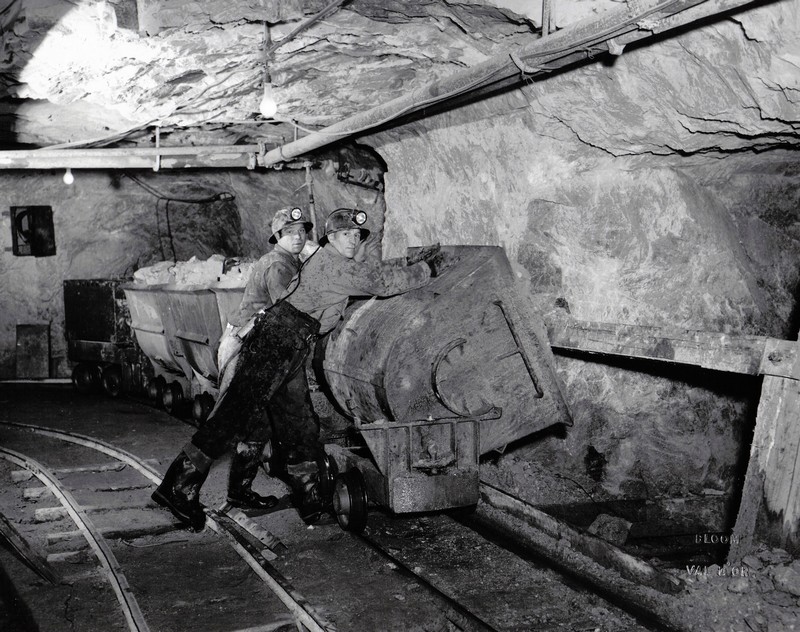 Two miners unloading a cart of crushed rock in the ore pass.