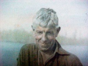 Sepia colourized photo of a smiling man with white hair and wearing a brown shirt.