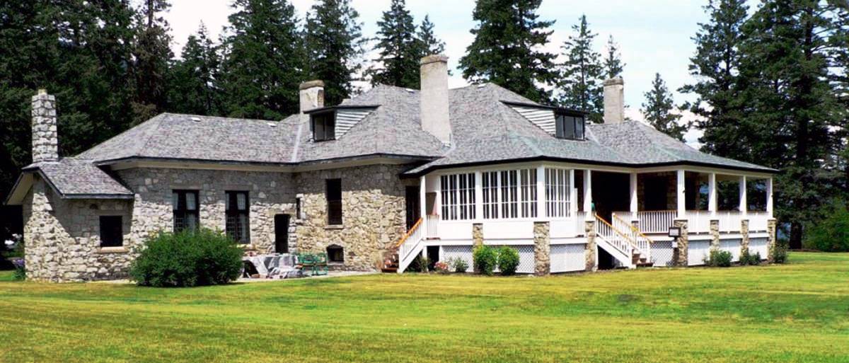 Colour photo of a large grey stone house with a white wooden verandah.