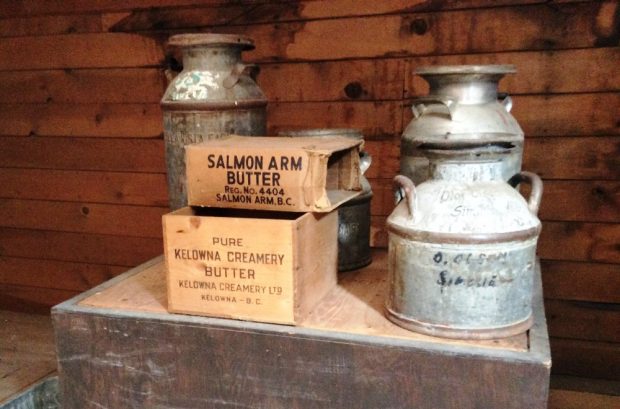 Colour photo of four milk cans, two butter boxes on a wooden stand.