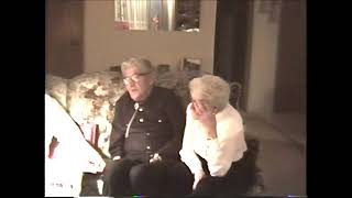 Colour photo of an older man and older woman sitting on a sofa looking at a photo album.