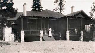 Black and white photo of a house with a screened porch. A woman wearing a white dress is standing on the steps.