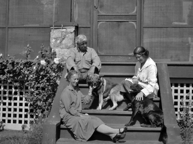 Black and white photo of a man and two women sitting on a porch step.