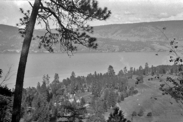 Black and white photo of a view looking down to buildings and a large lake.