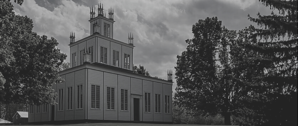 Black and white image of the Sharon Temple, a three story stacked square building surrounded by large maple trees.