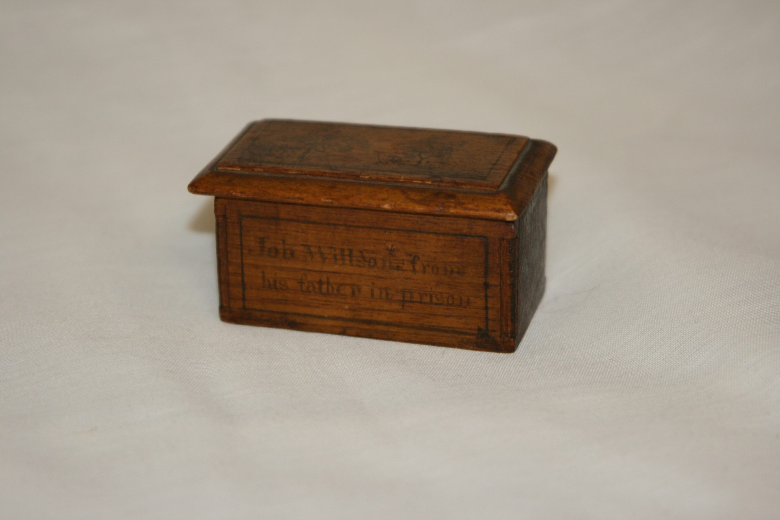 Small rebellion box mad by John David Willson for his son, Job Willson. The box has a sliding lid engraved with a picture of a small house with several trees. The sides of the box read "Lount and Matthews executed April 12, 1838" and "Job Willson from his father in prison"