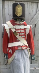 Photo d’une réplique d’un uniforme de l’armée britannique. La veste est rouge et le haut chapeau noir porte un insigne de sergent. 