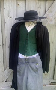 Photo d’une réplique des vêtements que pouvaient porter les rebelles : un chapeau à large bord, un veston noir, une chemise blanche en coton, un gilet vert et des pantalons gris. 