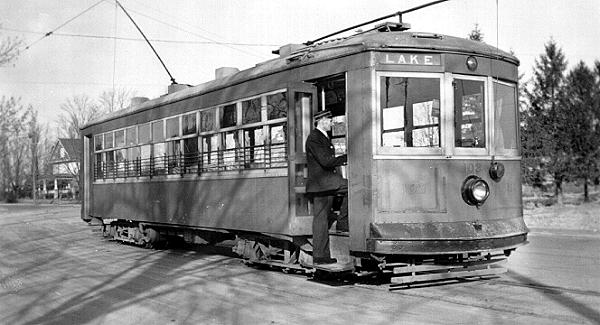 Black and white photograph of an electric street car and a person at the door. Lake is noted on the front of the electric street car.