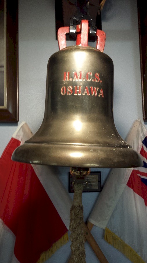 Colour photograph of a large brass bell from the HMCS Oshawa.