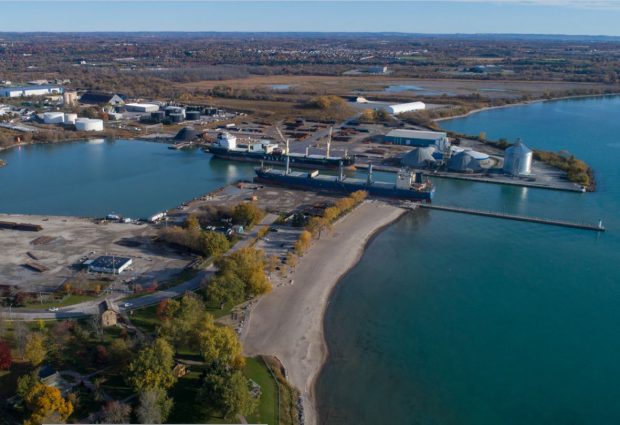 Colour aerial photograph of the land and water around the harbour. Two large ships are docked in the water basin.