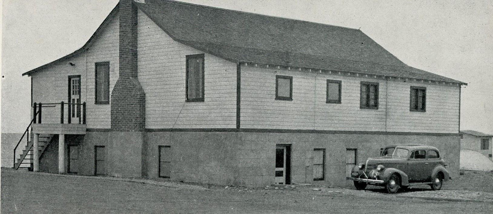 Black and white photograph of a building with a car parked behind.