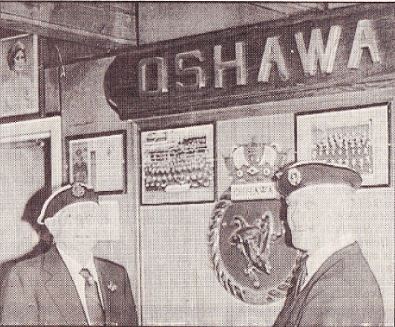 Sepia copy of a photograph of two people wearing caps standing near a sign that says Oshawa.