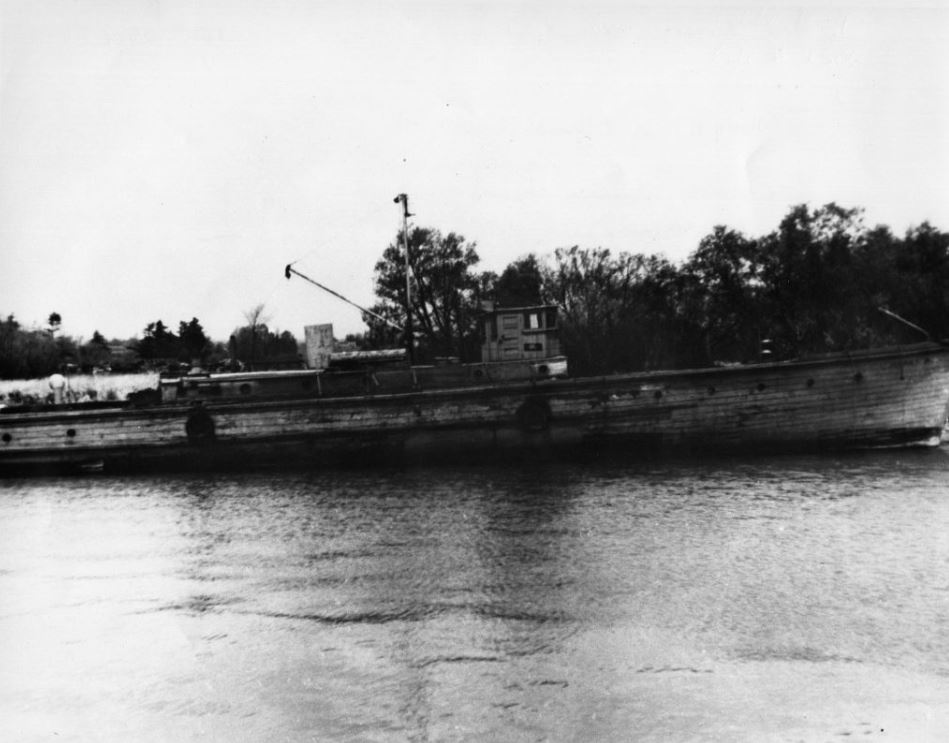 Black and white photograph of a long boat named, Harry H, on the water.