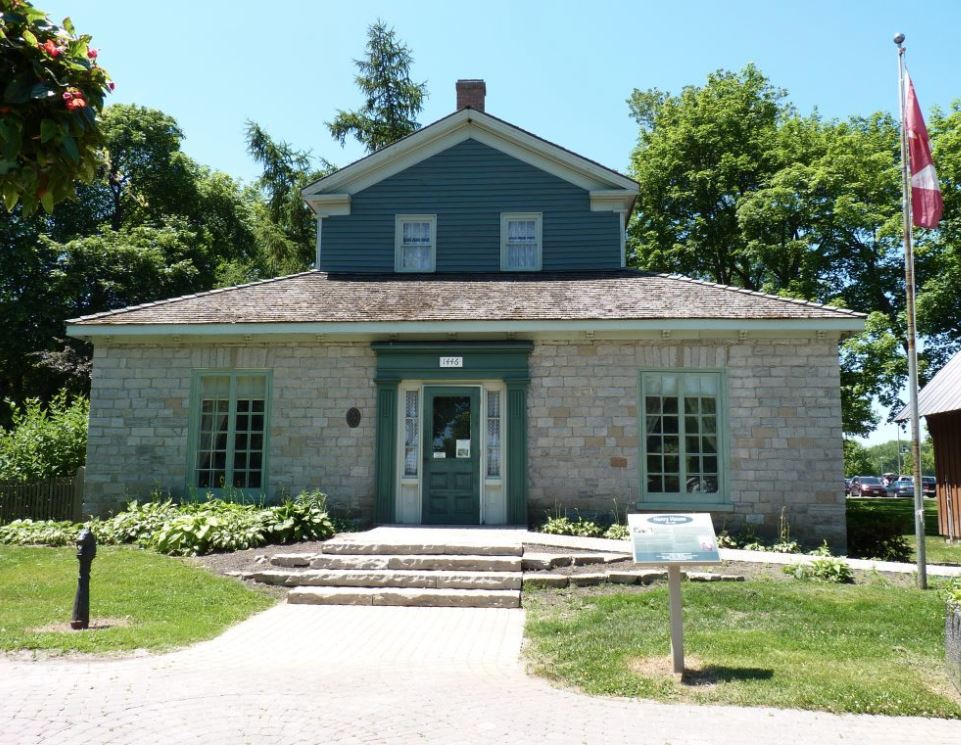 Colour photograph of a stone house with a second story that is painted green.