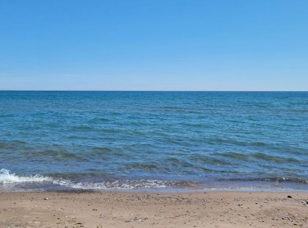 Colour photograph of a large body of water and sand.