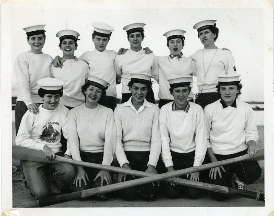 Black and white photograph of a group of people with two wooden oars in front.