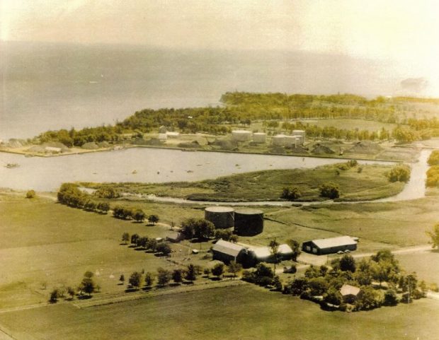 Colour aerial photograph of the land around the Oshawa Harbour before the Marina opened. There is a farm in the foreground and harbour buildings in the background.
