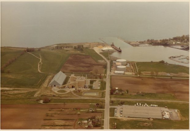 Colour aerial photograph of the land around the Oshawa Harbour. There are two large factories and a ship unloads raw sugar at the harbour.