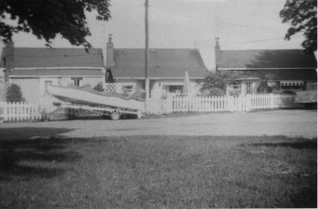 Black and white photograph of three cottages and a boat.